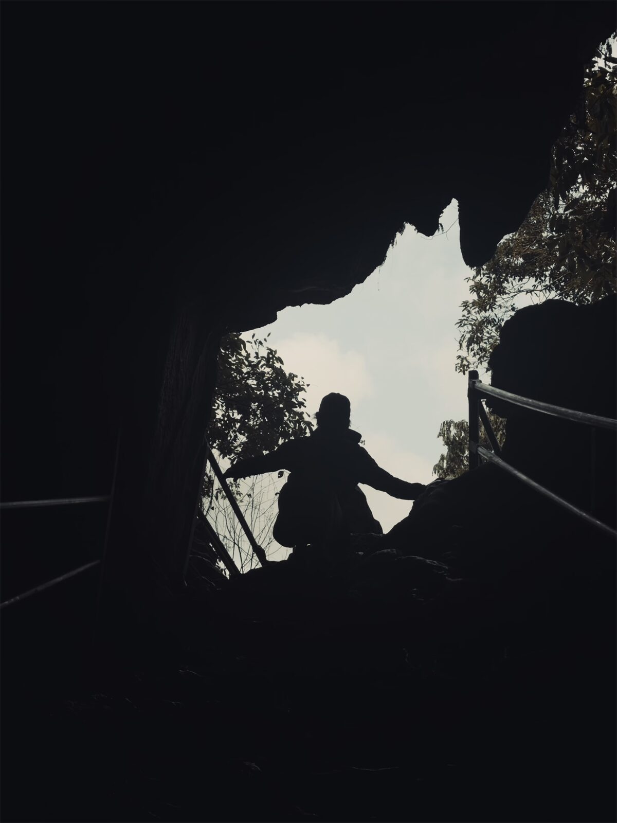 Looking up at the mouth of a cave: the silhouette of a hiker against the bright sky — the light is outside, the darkness is at your feet, and the body is just about to walk in