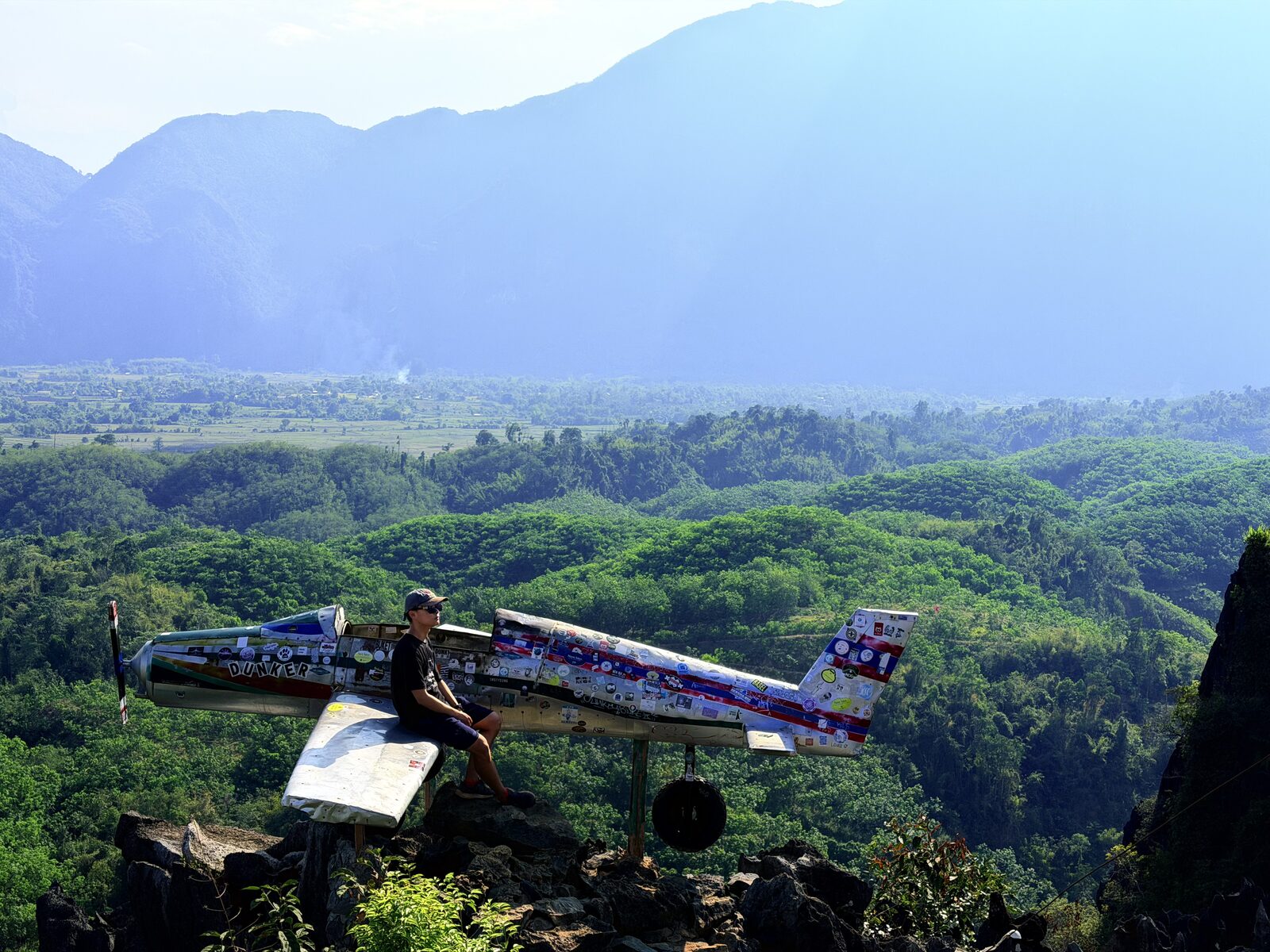 The “Dunker” plane installation on top of Nam Xay mountain in Vang Vieng — covered in stickers from travelers around the world, with layer after layer of karst mountains and rice paddies behind it. A joy already certified by the footsteps of countless strangers
