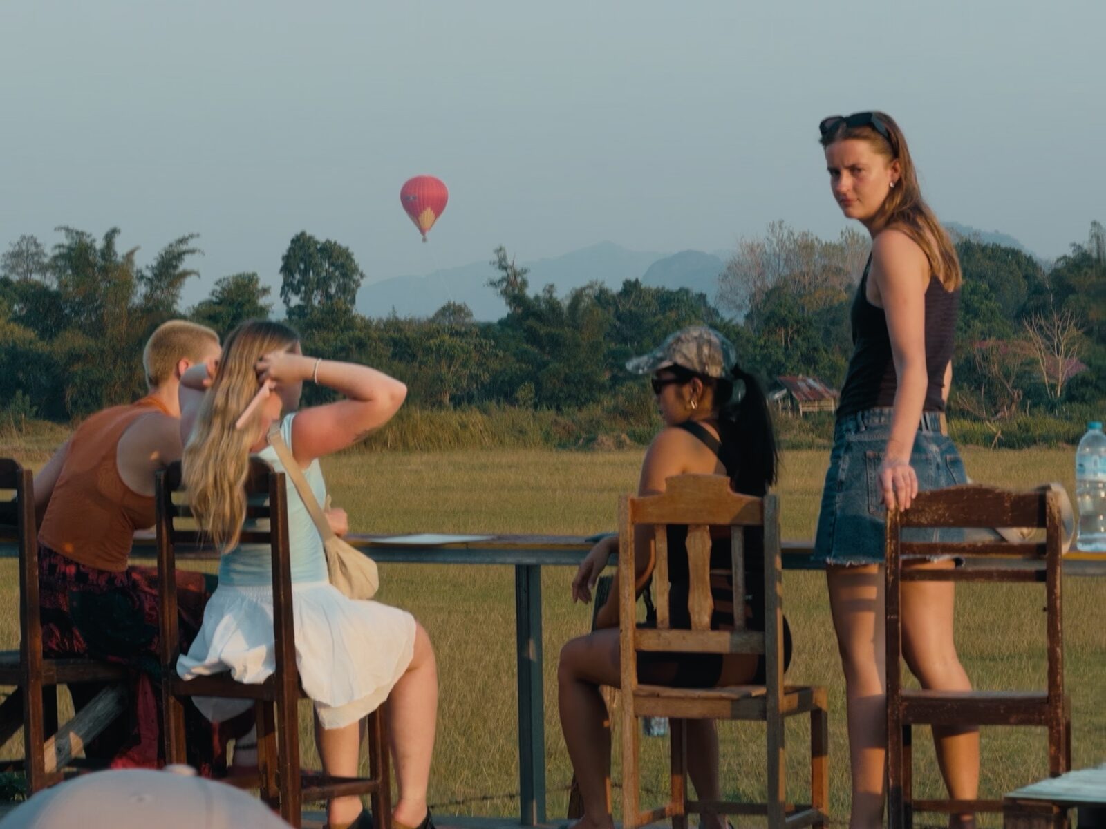 Dusk in Vang Vieng — a hot-air balloon drifts above the rice paddies in the distance, a few travelers sitting at a wooden table. One of the last frames before I left, and the very frame that floats up later, every time I think back on the word “reluctance”